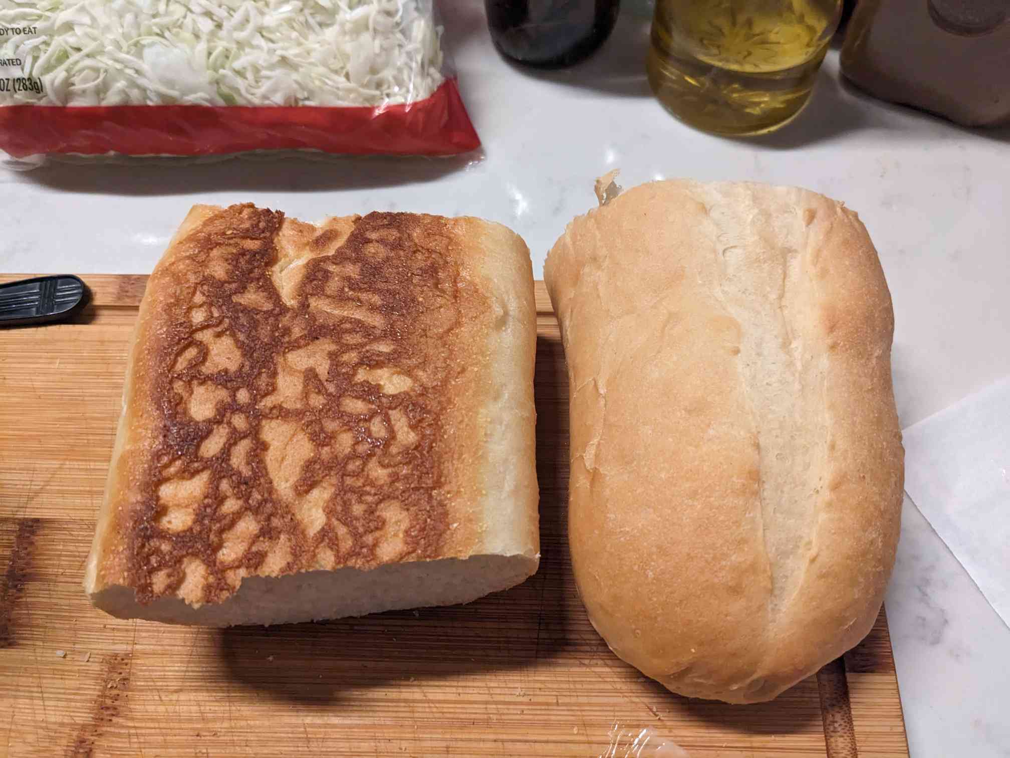 A loaf of Cuban bread sliced in half, displaying the top and bottom of the loaf. It is on a wooden cutting board on a white counter